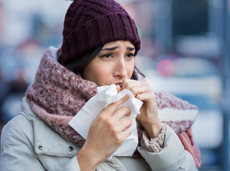 Млада жена, облечена със зимни дрехи, кашля в салфетка